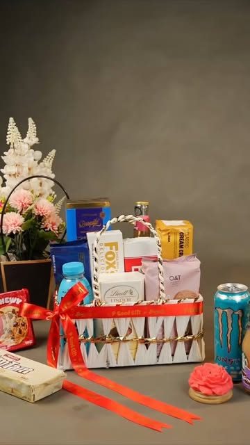 A Brown Bascaed basket with chocolates, a drink can and a red ribbon