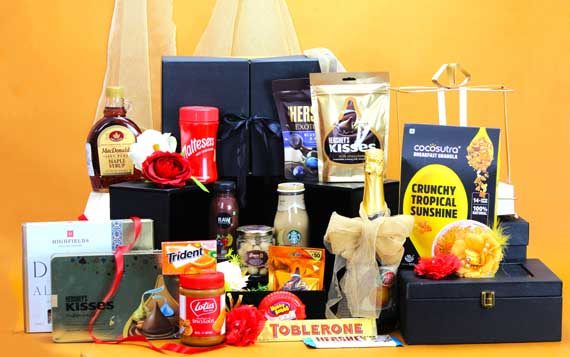 Brown Bascaed gift hamper with chocolates, spreads and roses on a mustard backdrop